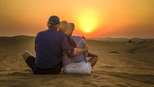 Un uomo e una donna seduti nel deserto a guardare il tramonto di Sahara Desert Camp a Merzouga