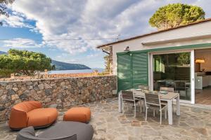 een patio met een tafel en stoelen en een stenen muur bij Apartment Mare di Spartaia in Procchio