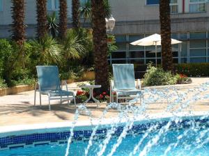 zwei Stühle und ein Sonnenschirm neben einem Pool in der Unterkunft Hotel Air Penedès in Vilafranca del Penedès