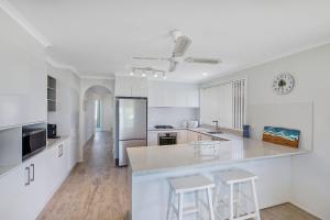 Una cocina blanca con encimera y taburetes. en Seashells on Eloora, en Long Jetty