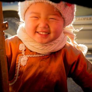 Ein kleines Mädchen mit Hut und orangefarbener Jacke. in der Unterkunft UB Guesthouse & Tours in Ulaanbaatar