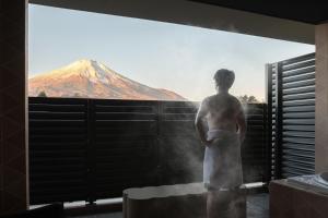 a man standing in front of a window looking at a mountain at Mt Fuji View and Private Sauna Ryokan Shizuku in Yamanakako