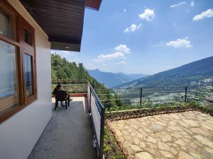 a person sitting in a chair on a balcony looking out at the mountains at Ekaant Orchard Retreat , A Serene Homestay in Nārkanda