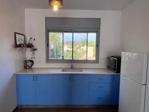 a kitchen with blue cabinets and a sink and a window at אגמון החולה in Lahavot HaBashan