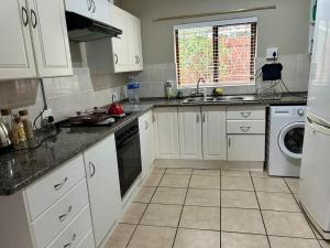 a kitchen with white cabinets and a washer and dryer at Garden View Seaside Chalet in Hibberdene