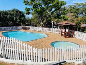 a white fence surrounds a swimming pool with a gazebo at Garden View Seaside Chalet in Hibberdene