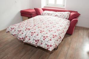 a red couch with a bed with a flowered blanket at Apartment Bon Voyage in Maribor