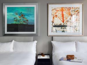 two beds in a hotel room with two paintings on the wall at The Olsen Melbourne Art Series in Melbourne
