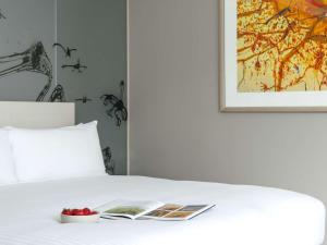 a bed with a book and a bowl of fruit on it at The Olsen Melbourne Art Series in Melbourne
