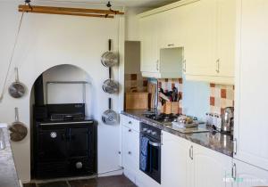 a kitchen with white cabinets and a black stove top oven at Stone Hall Mill Cottage - Tranquil Countryside Haven in Pembrokeshire in Saint Lawrence