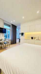 a white bedroom with a large bed and a kitchen at Studio Fischer à la Pétrusse 001 in Luxembourg