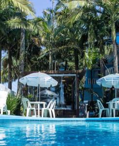 a swimming pool with white chairs and umbrellas at Pousada Bella Praia in Torres