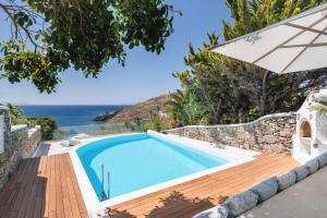 a swimming pool with an umbrella and the ocean in the background at Zegna Pool Villa, Three Bedrooms in Mikonos