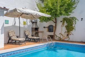 a pool with two chairs and an umbrella next to a house at Casa rural VISTABLANCA en una sola planta con bonitas vistas y piscina - Junto a la capital y la Alhambra in Cenes de la Vega