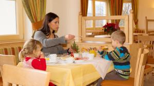 a woman and two children sitting at a table eating food at Pension Steiermark in Schladming