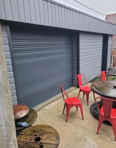 eine Terrasse mit roten Stühlen, einem Tisch und einer Garage in der Unterkunft Chambre lit 2 personnes in Saint-Martin-lez-Tatinghem