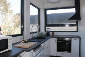 a kitchen with white cabinets and a sink and two windows at L'idylle - maison a la mer in Quiberville