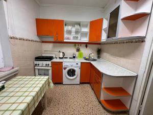 una pequeña cocina con armarios naranjas y lavadora en Nuri, en Karakol