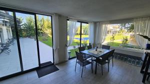 Un comedor con mesa y sillas y grandes ventanales. en Neferprod Apartments - IS - CAM 01, en Timisoara