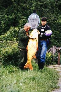 deux hommes détenant un grand poisson devant un panneau dans l'établissement Erdész Vendégház, à Uppony
