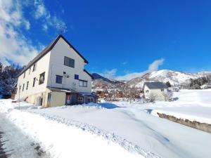 a house in the snow with mountains in the background at Hakuba Norikura Wakaguri Guesthouse in Otari