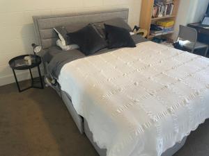 a bed with a white comforter and a table with a chair at Luxury townhouse with aircon, huge balcony & hot tub in Auckland