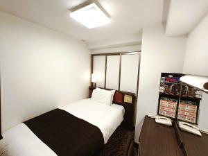 a small room with a bed and a desk with a phone at APA Hotel Tokushima Ekimae in Tokushima