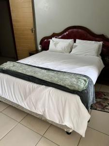 a bed with white sheets and a wooden headboard at Rural Villa Guesthouse in Naledi