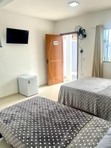 a bedroom with two beds and a television and a door at Suitella in Cabo Frio +13 photos
