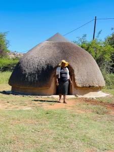 une femme debout devant une cabane de toit de chaume dans l'établissement Indlondlo Cultural Village, à Cato Ridge