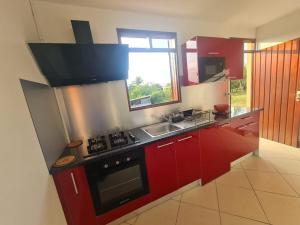 a kitchen with red cabinets and a stove and a sink at On Ti Flè Gîte in Anse-Bertrand