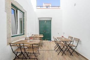 a room with wooden tables and chairs and a green door at Casa dos Cucos in Ericeira