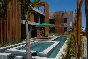 a pool with an umbrella and a palm tree next to a building at Flats Beira-Mar na Rota dos Milagres - Essence Tatuamunha in Pôrto de Pedras