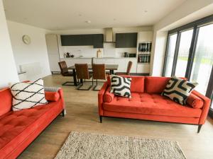 a living room with two red couches and a kitchen at Glynllifon 3 in Llanallgo