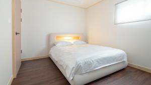 a white bedroom with a bed with a light on it at Jeju Staysosoheon dokchae pension in Jeju