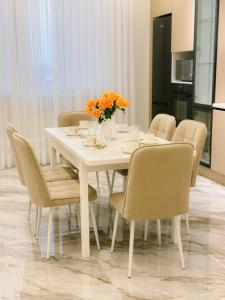 einen weißen Tisch mit Stühlen und eine Vase mit orangefarbenen Blumen in der Unterkunft В шикарном районе Атырау возле дворца ЦЕНТР АБАЯ New City от аэропорта 3 минуты in Atyrau