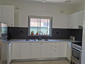 a white kitchen with a sink and a window at Three Bedrooms House in Chullora