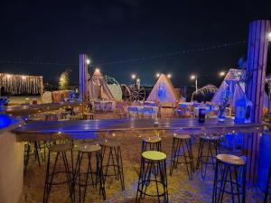 a bar with stools in front of tents at night at חאן הכנסת אורחים B''H village שומר שבת in Nevatim