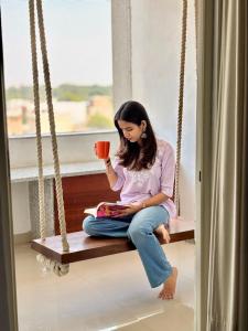una chica sentada en un columpio sosteniendo una taza de café en Lotus Diamerisma - 2BHK Furnished Apartment in Jodhpur - Peaceful Retreat Away from City Traffic, en Jodhpur