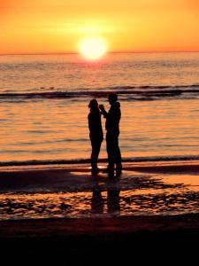 dwie osoby stojące na plaży o zachodzie słońca w obiekcie Dune Bep w mieście Schiermonnikoog