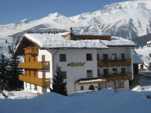 a building with snow on top of it in front of mountains at Alpenhof Pension-Garni in Nauders