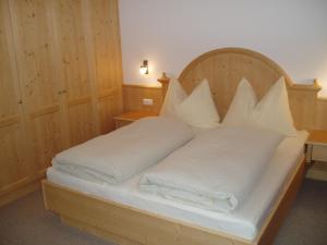 1 dormitorio con cama de madera con sábanas y almohadas blancas en Appartmenthaus Aschaber, en Westendorf
