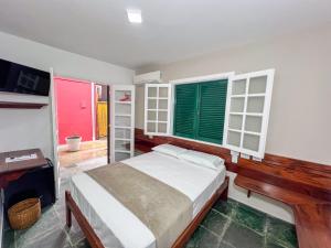 a bedroom with a bed and a desk and windows at Pousada Promessa Amanay antigamente Ubatuba Guest House in Ubatuba