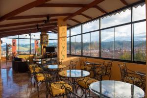 un restaurante con mesas, sillas y ventanas grandes en Hostal Qolqampata, en Cusco