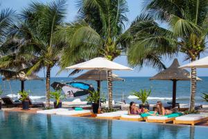 a pool at a resort with palm trees and people sitting at Mana Mui Ne Beach Resort & Spa in Mui Ne