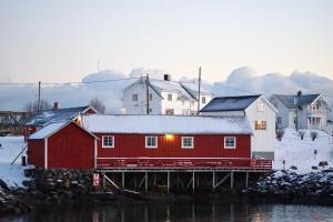 a red house with snow on it next to some buildings at Anitas Waterfront Cabins in Reine