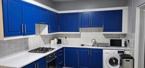 a kitchen with blue cabinets and a washing machine at Glebe House - 2 Bedroom Beautiful House that sleeps 6, with Free Private Parking, Easy Access to City Centre, and Near the Motorway in Moston