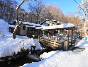 une cabine dans la neige à côté d'une rivière dans l'établissement Kose Onsen, à Karuizawa