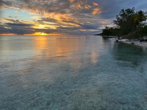 a view of a beach with the sun setting over the water at Dôme sur la Passe de Tiputa in Rangiroa +7 photos