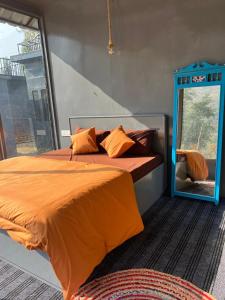 a bed with an orange comforter and a mirror at Tattvammasi Stay in Bajaura